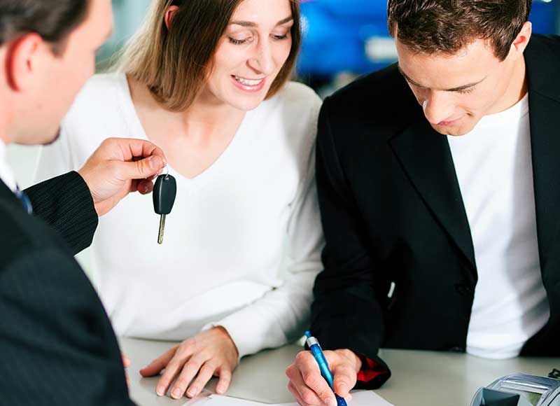 Couple signing car purchase papers as dealer hands over car key