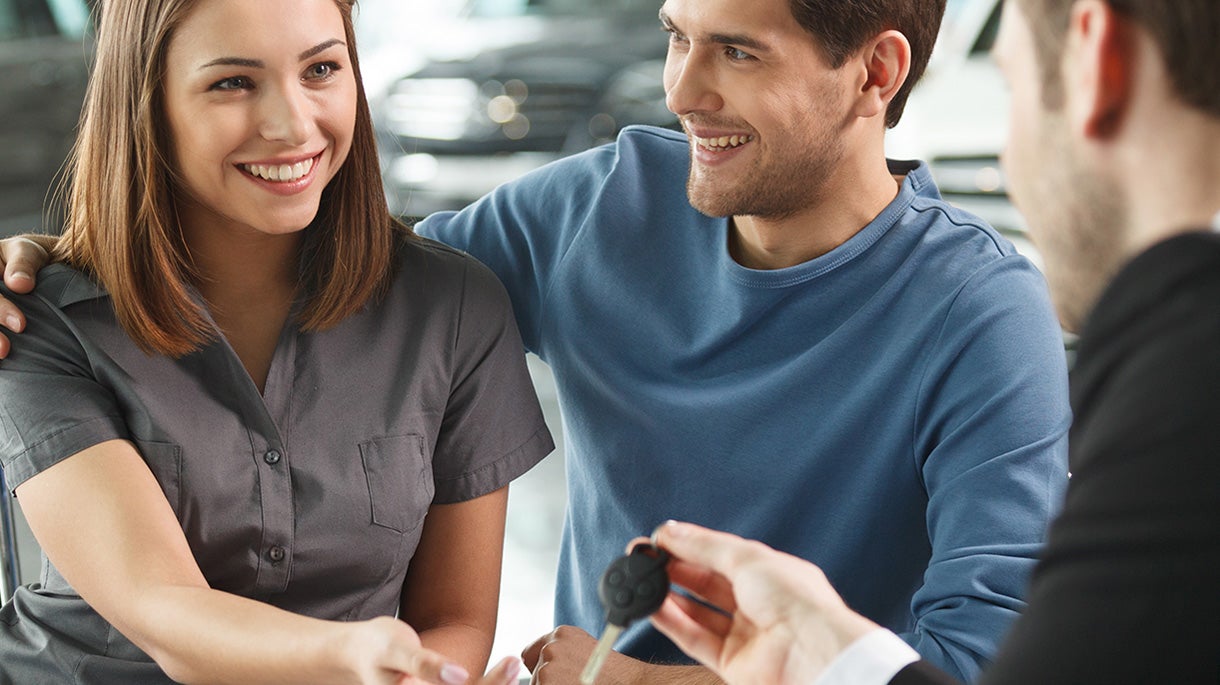Smiling couple receiving car key from dealer